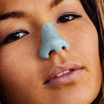 Load image into Gallery viewer, A young woman is wearing blue Nöz Sunscreen on her nose and is looking at the camera.
